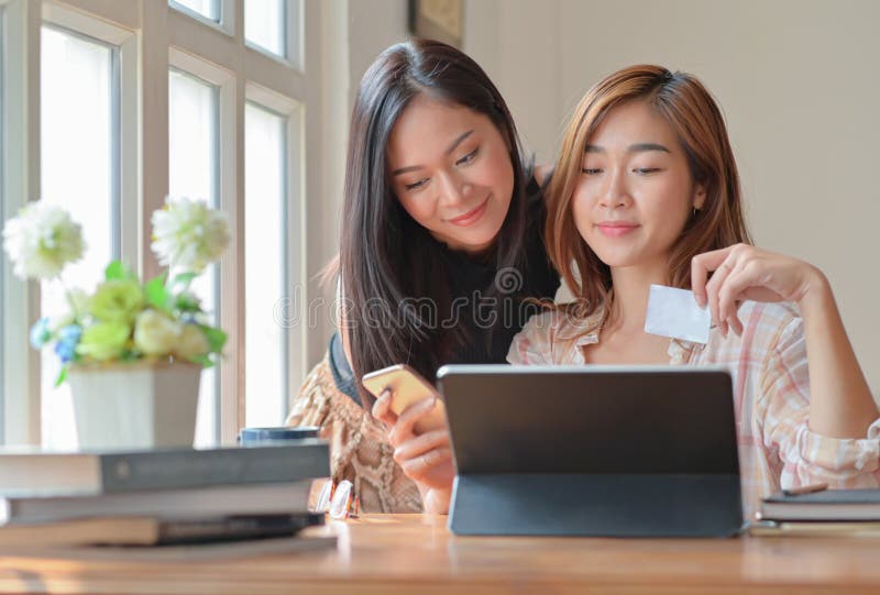 Två tonårsflickor handlar online med en tablett hemma för att beställa och betalar online med kreditkort arkivfoto