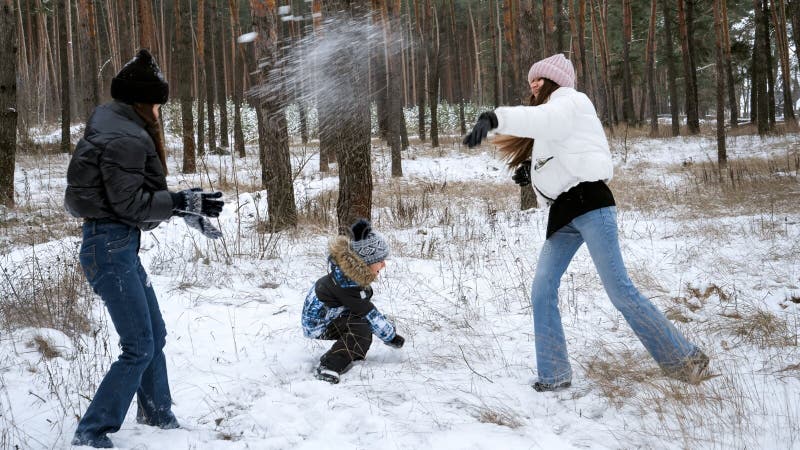Två tonårsflickor leker med liten pojke i snö och kastar snöbollar. Personer som leker utomhus under vintersemester och semester arkivbild