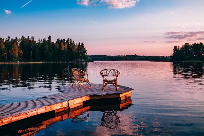 Två trästolar på en wood pir som förbiser en sjö på solnedgången royaltyfria foton Två trästolar på en wood pir som förbiser en sjö på solnedgången royaltyfria foton