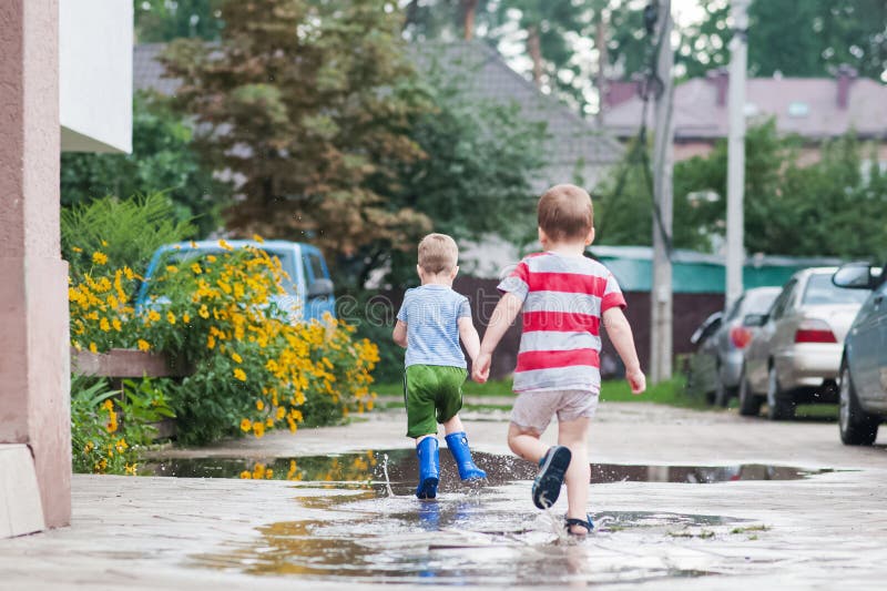 Två unga barn som går igenom Rain Puddles i sommargrannskapet arkivfoto