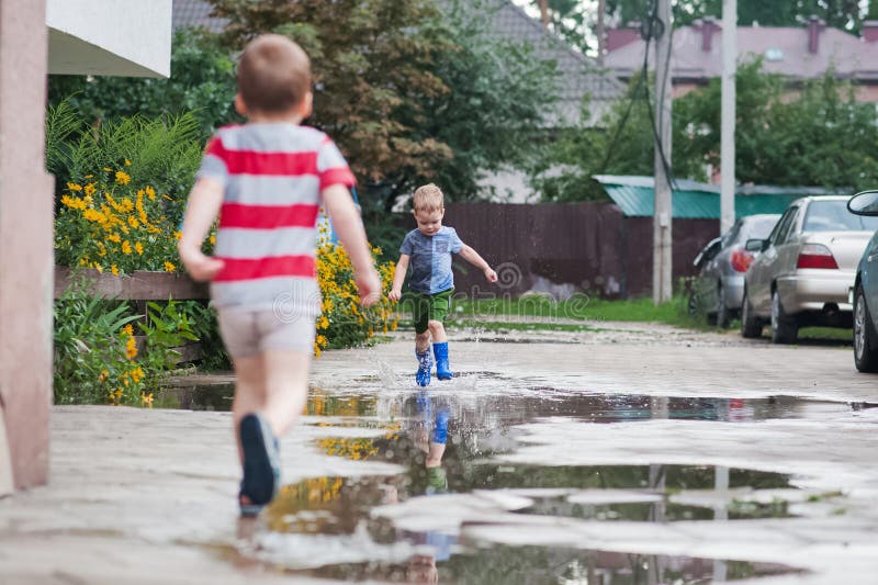 Två unga barn som går igenom Rain Puddles i sommargrannskapet arkivbild