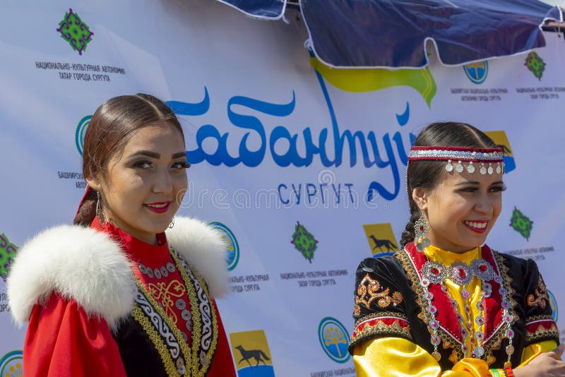 Två unga kvinnor i nationell Bashkir kläder och bak dem ettspråk ’Sabantuy Surgut ’, arkivfoto Två unga kvinnor i nationell Bashkir kläder och bak dem ettspråk ’Sabantuy Surgut ’, arkivfoto