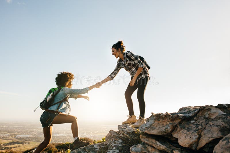 Young women helping friend to climb up the rock. Two young females hiking in nature. Young women helping friend to climb up the rock. Two young females hiking in nature.