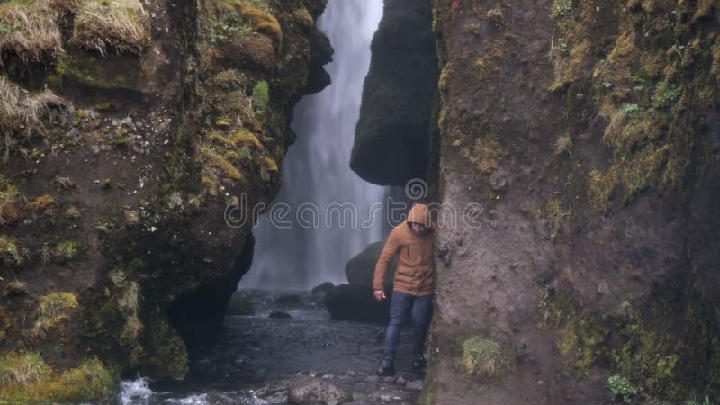 Två unga turister som undersöker den kraftiga vattenfallet Gljufrabui i Island Man och kvinna i regnrock som går i regn