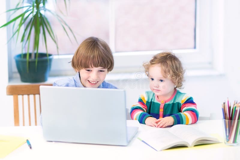 Två ungar som spelar med bärbar datorsammanträde på det vita skrivbordet