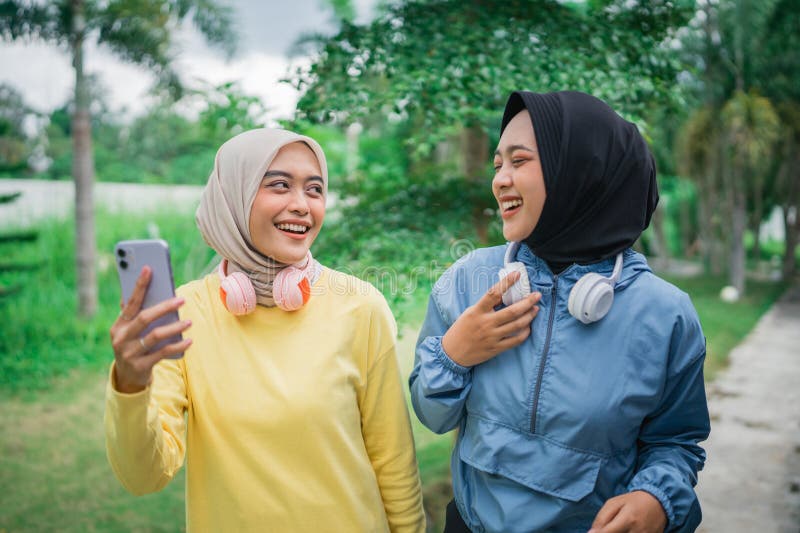 Två vackra hijab-flickor som chattar och håller en smartphone medan de går royaltyfri foto
