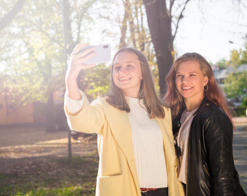 Två vackra unga flickor som tar selfie på telefon i soliga höstpark royaltyfri foto