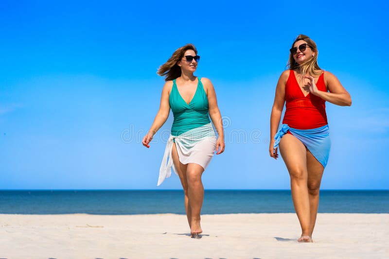 Två vackra unga kvinnor som har baddräkter och pareo och som pratar på vit sandstrand fotografering för bildbyråer