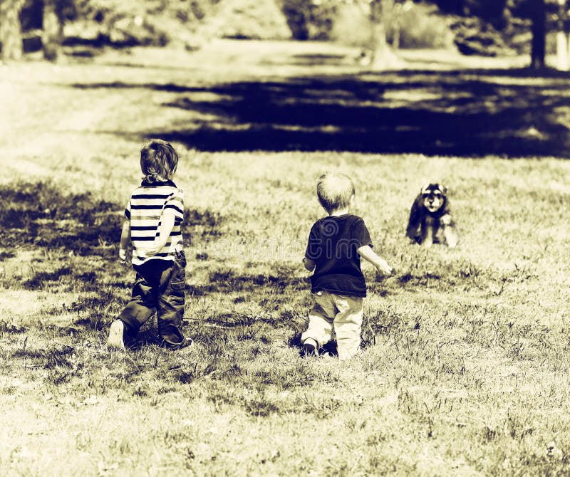 Två Young Boys på en parkera som att närma sig en hund - Sepia arkivfoton Två Young Boys på en parkera som att närma sig en hund - Sepia arkivfoton