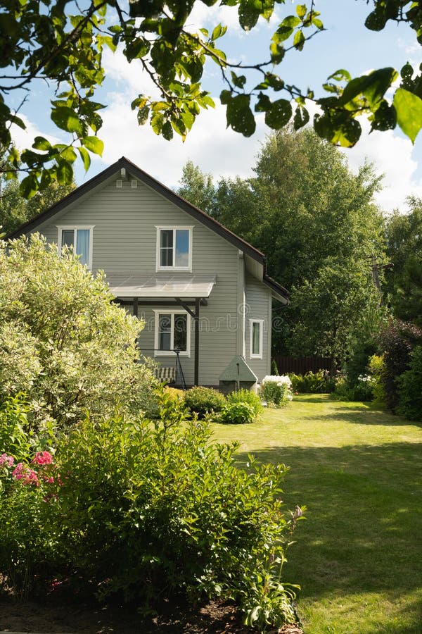 Tvåvåvåningshus på landsbygden under sommaren med buskgräta träd och blommande träd. Ryska arkivfoton