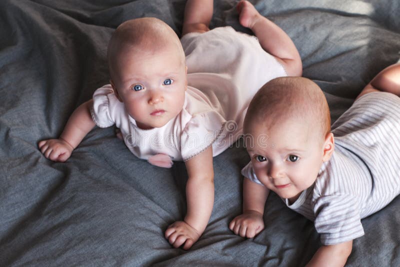 Twee aanbiddelijke babes een jongen en een meisje spelen op het bed op een grijze achtergrond Broer en zuster Tweelingen Selectie stock fotografie Twee aanbiddelijke babes een jongen en een meisje spelen op het bed op een grijze achtergrond Broer en zuster Tweelingen Selectie stock fotografie