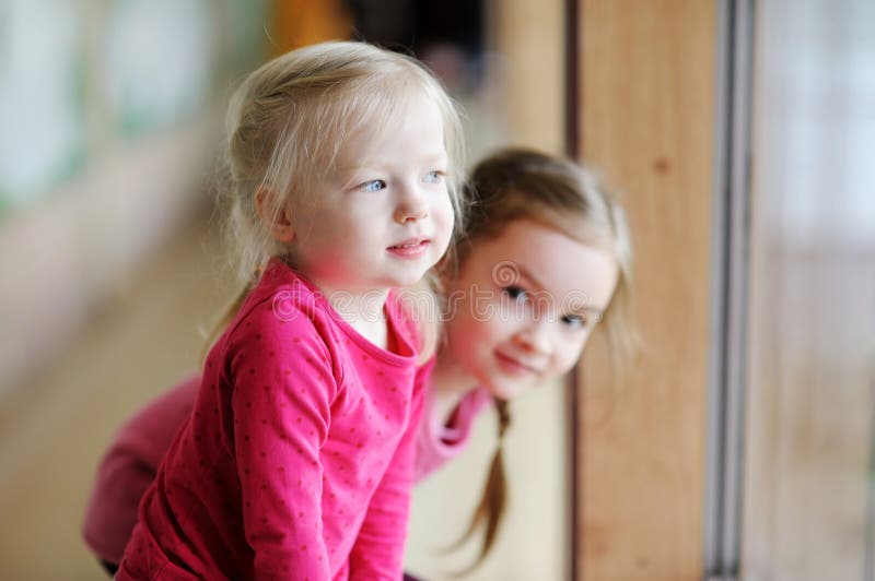 Twee aanbiddelijke kleine zusters door het venster royalty-vrije stock fotografie Twee aanbiddelijke kleine zusters door het venster royalty-vrije stock fotografie