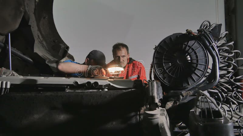 Twee autowerktuigkundige met lamp streeft naar het breken van motor van vrachtwagen