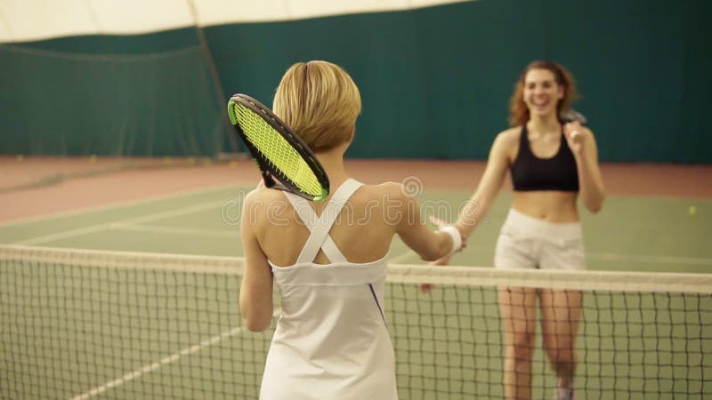 Twee concurrerende vrouwelijke tennisspelers begroeten cheerfuly elkaar, dient de schok het behandelde tennisbaangebied in