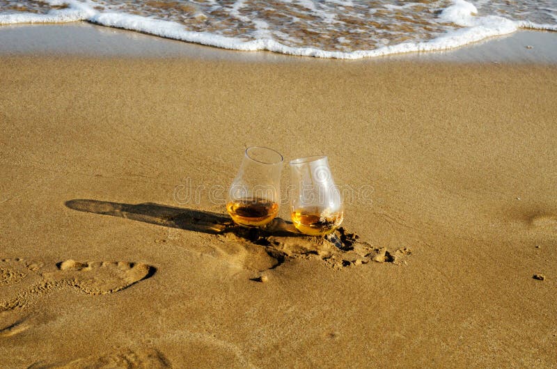 Twee die glazen whisky kiezen mout op het zand uit door wav wordt gewassen stock fotografie Twee die glazen whisky kiezen mout op het zand uit door wav wordt gewassen stock fotografie