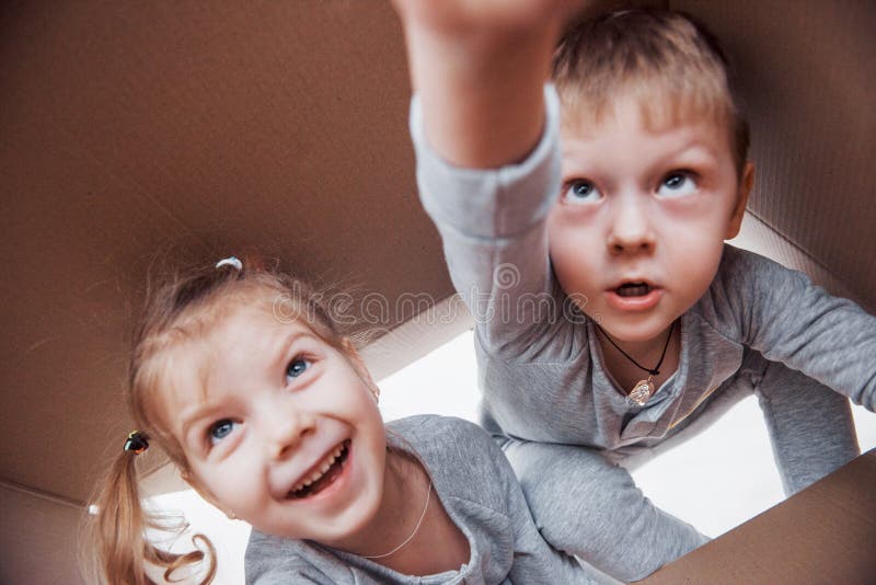Twee een klein jonge geitjesjongen en een meisje die een kartondoos openen en in het midden van het beklimmen De kinderen hebben stock afbeelding Twee een klein jonge geitjesjongen en een meisje die een kartondoos openen en in het midden van het beklimmen De kinderen hebben stock afbeelding