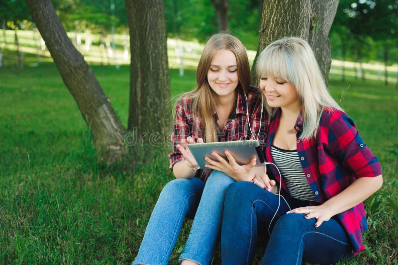 Twee gelukkige vrienden die media zoeken stellen online in een laptop zitting op het gras in een park tevreden royalty-vrije stock fotografie Twee gelukkige vrienden die media zoeken stellen online in een laptop zitting op het gras in een park tevreden royalty-vrije stock fotografie