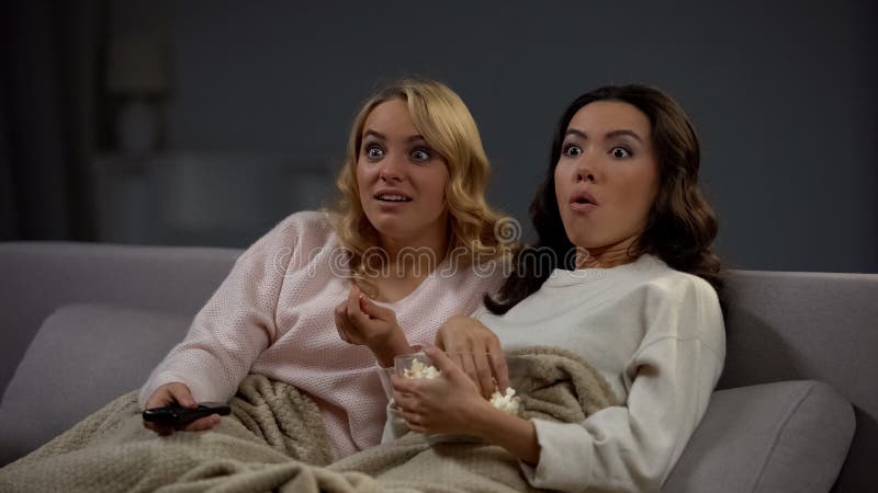 Twee geschokte vrouwen die popcorn eten en op interesserend TV programma, rust letten royalty-vrije stock afbeeldingen Twee geschokte vrouwen die popcorn eten en op interesserend TV programma, rust letten royalty-vrije stock afbeeldingen