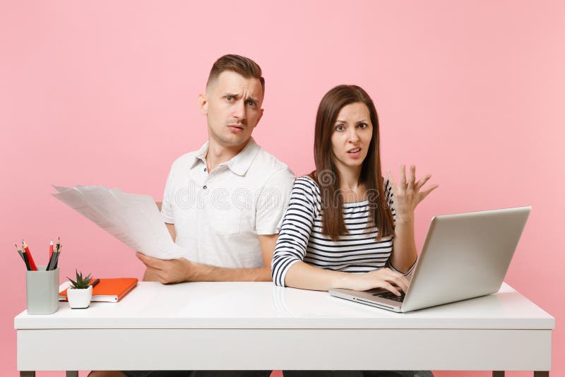 Twee glimlachende bedrijfsvrouwenman collega's zitten werk bij wit bureau met eigentijdse die laptop op pastelkleur roze achtergr stock fotografie Twee glimlachende bedrijfsvrouwenman collega's zitten werk bij wit bureau met eigentijdse die laptop op pastelkleur roze achtergr stock fotografie