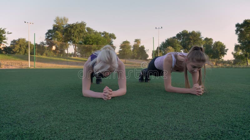 Twee het doen van de jonge mooie vrouw plankoefening op voetbalgebied in park tijdens ochtend, geschiktheid modelleert het uitoef
