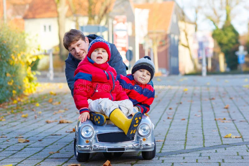 Twee het kleine van de jonge geitjesjongens en vader spelen met auto, in openlucht stock fotografie Twee het kleine van de jonge geitjesjongens en vader spelen met auto, in openlucht stock fotografie