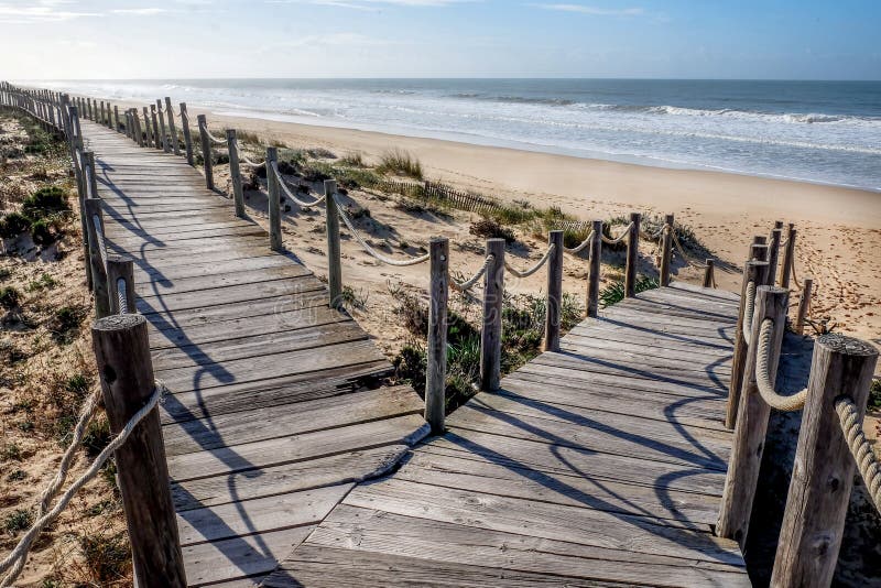 Looking down two wooden decking pathways forming a fork in the road, both heading down to a sweeping sandy beach with the blue sea and blue sky in front  Praia Da Lagoa, Algarve, Portugal. Looking down two wooden decking pathways forming a fork in the road, both heading down to a sweeping sandy beach with the blue sea and blue sky in front  Praia Da Lagoa, Algarve, Portugal