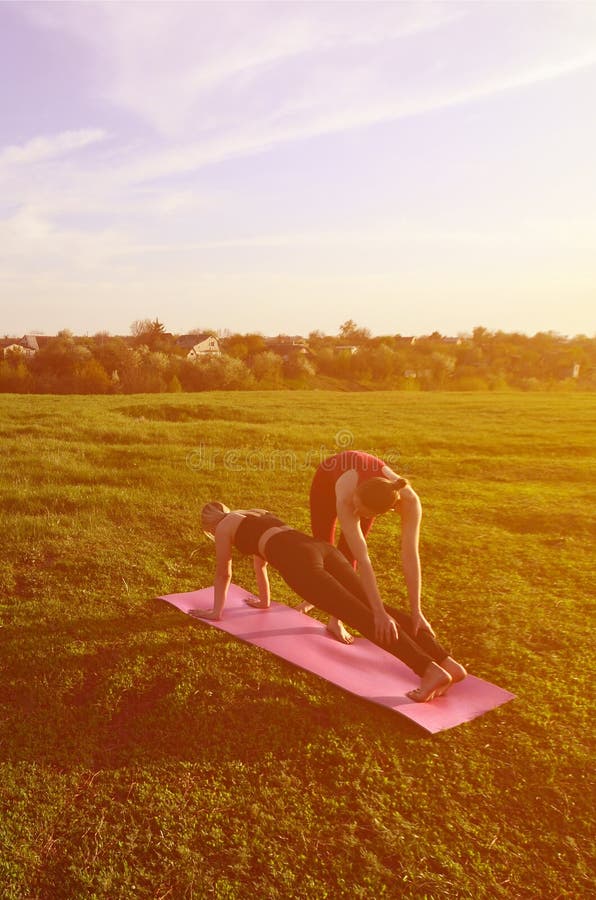 Twee jonge blonde meisjes in sporten past praktijkyoga op een schilderachtige groene heuvel aan royalty-vrije stock foto Twee jonge blonde meisjes in sporten past praktijkyoga op een schilderachtige groene heuvel aan royalty-vrije stock foto