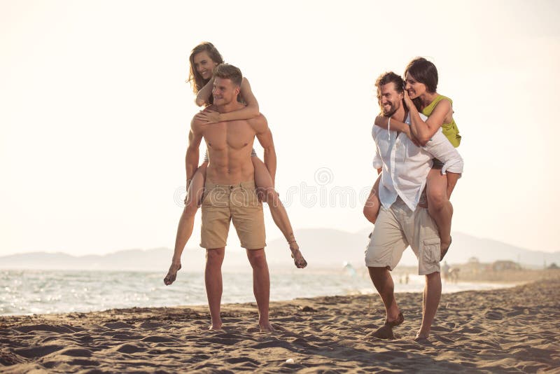 Twee jonge mensen die hun meisjes geven vervoeren per kangoeroewagen ritten bij het strand stock fotografie Twee jonge mensen die hun meisjes geven vervoeren per kangoeroewagen ritten bij het strand stock fotografie