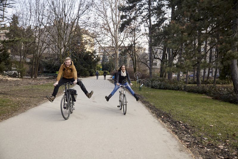 Twee jongeren, 20-29 jaar die oud, een fiets in een park met uitgerekt, dwaze benen berijden, en pret hebben lachen stock afbeelding Twee jongeren, 20-29 jaar die oud, een fiets in een park met uitgerekt, dwaze benen berijden, en pret hebben lachen stock afbeelding