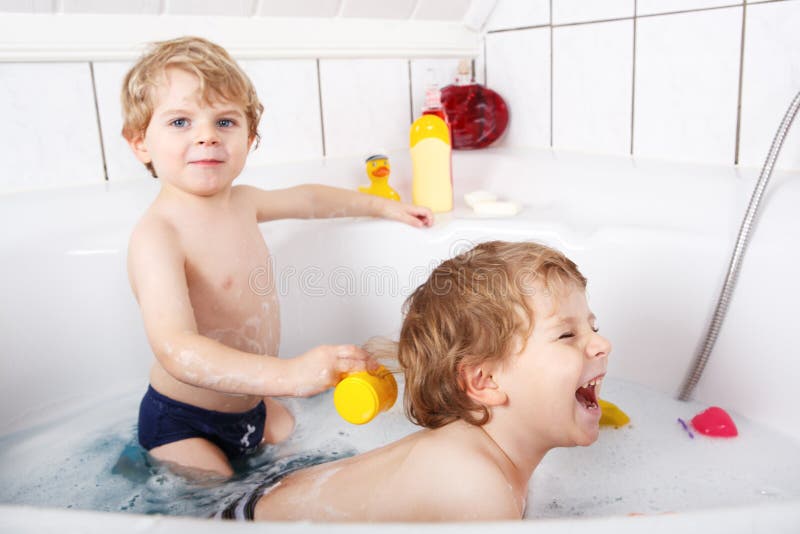Twee kleine tweelingenjongens die pret met water hebben door bad in bedelaars te nemen stock foto Twee kleine tweelingenjongens die pret met water hebben door bad in bedelaars te nemen stock foto