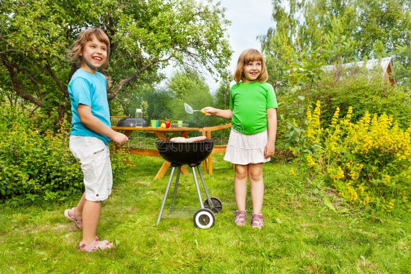 Twee kleine zusters die zich dichtbij BBQ en het roosteren bevinden stock afbeeldingen Twee kleine zusters die zich dichtbij BBQ en het roosteren bevinden stock afbeeldingen