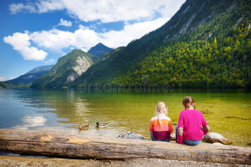 Twee leuke zusters die van de mening van donkergroene die wateren van Konigssee genieten, als het diepste en schoonste die meer v royalty-vrije stock afbeeldingen Twee leuke zusters die van de mening van donkergroene die wateren van Konigssee genieten, als het diepste en schoonste die meer v royalty-vrije stock afbeeldingen