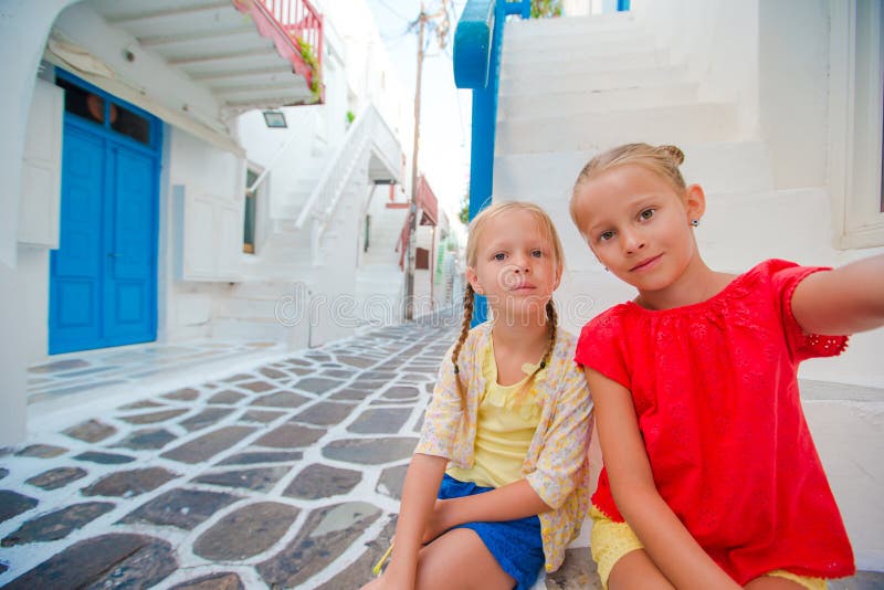 Twee meisjes die selfie foto in openlucht in Grieks dorp op smalle straat nemen stock fotografie Twee meisjes die selfie foto in openlucht in Grieks dorp op smalle straat nemen stock fotografie