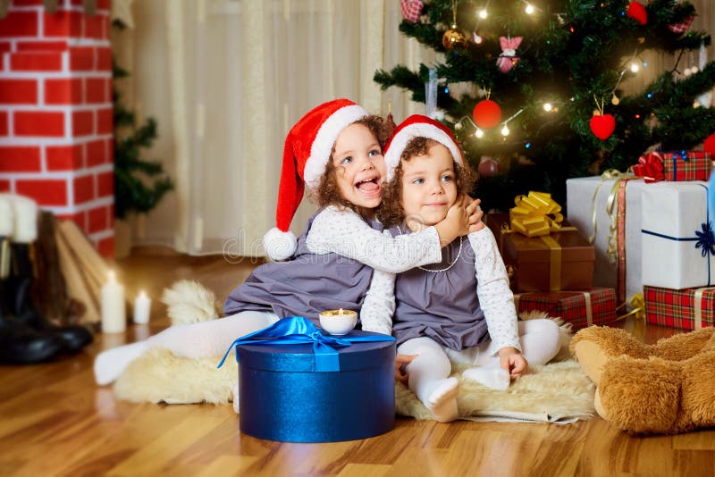 Twee meisjes in kappen van Santa Claus-zitting op de vloer weten royalty-vrije stock foto Twee meisjes in kappen van Santa Claus-zitting op de vloer weten royalty-vrije stock foto