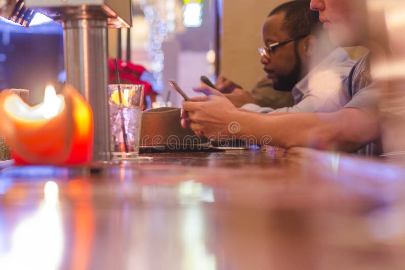 Twee Mensen die Tussen verschillende rassen bij een Bar zitten die Hun Telefoons bekijken stock foto Twee Mensen die Tussen verschillende rassen bij een Bar zitten die Hun Telefoons bekijken stock foto