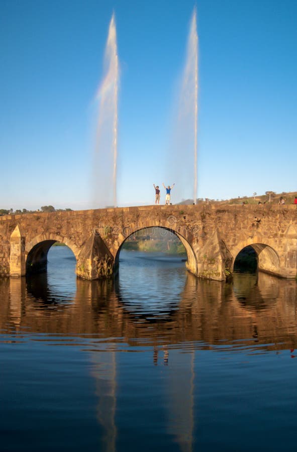 Two persons people stainding on a stone arch bridge with fountain and reflection. Two persons people stainding on a stone arch bridge with fountain and reflection