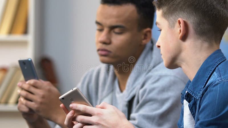 Twee middelbare schooljongens die sociale media plaats op smartphones doorbladeren, mobiele verslaving
