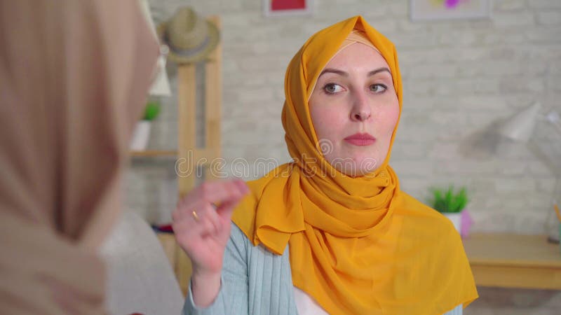 Twee mooie dove jonge Moslimvrouwen in hijabs die met Gebarentaal in de woonkamer dicht omhoog van het huis spreken