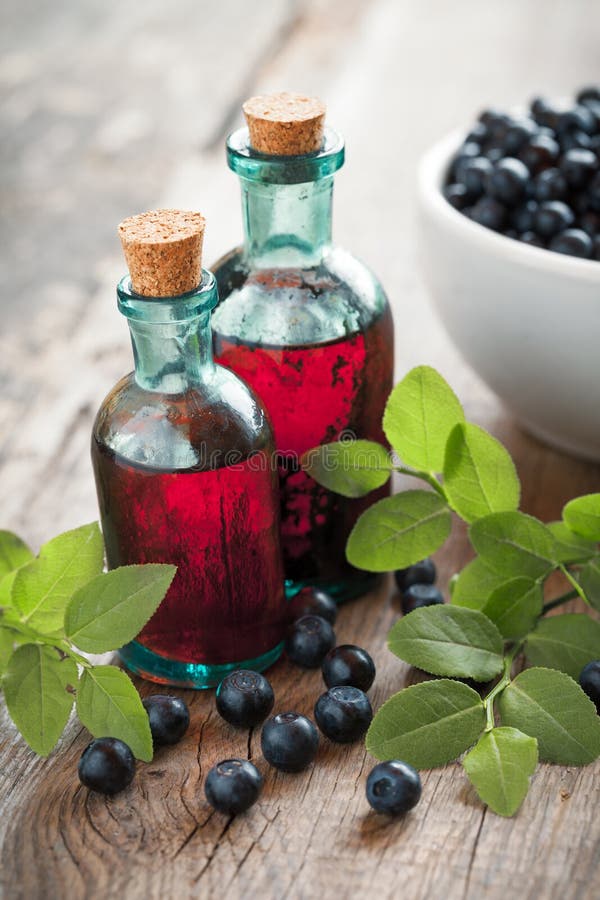 Two vintage bottles of tincture or cosmetic product and bowl with blueberries on wooden table. Two vintage bottles of tincture or cosmetic product and bowl with blueberries on wooden table.