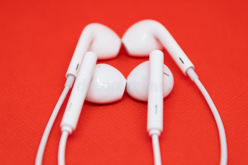 Twee paren witte hoofdtelefoons dicht bij elkaar op rode achtergrond, één paar oortelefoons is vaag stock fotografie Twee paren witte hoofdtelefoons dicht bij elkaar op rode achtergrond, één paar oortelefoons is vaag stock fotografie