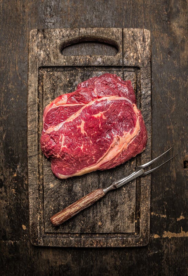 Twee ruw rundvlees ribeye lapje vlees met vleesvork op donkere rustieke houten uithalende raad stock afbeeldingen Twee ruw rundvlees ribeye lapje vlees met vleesvork op donkere rustieke houten uithalende raad stock afbeeldingen