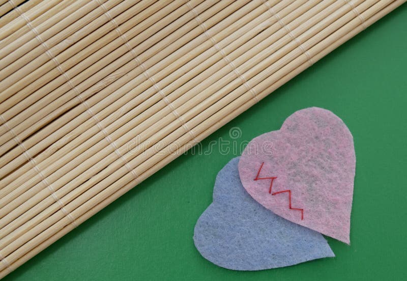 two fabric hearts sewn together on a green background. the background is divided diagonally. two fabric hearts sewn together on a green background. the background is divided diagonally