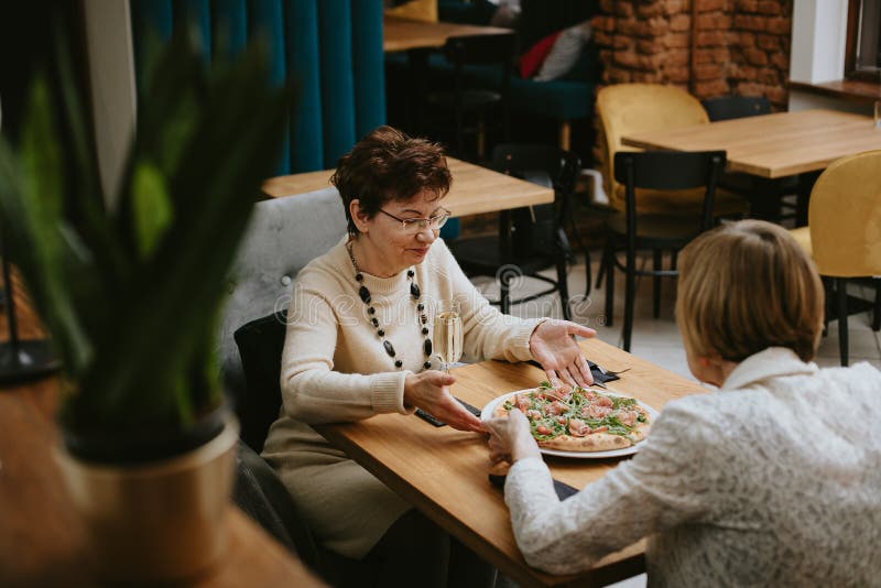 Twee vrienden ontmoeten elkaar in restaurant dressy dames in de restauranttijd en eten lekkere pizza aan tafel in café hall. oud