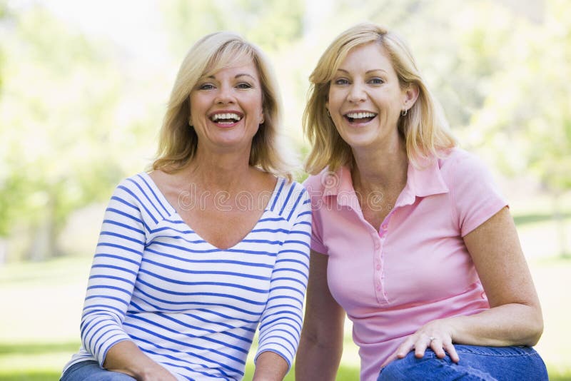 Twee vrouwen die in openlucht het glimlachen zitten