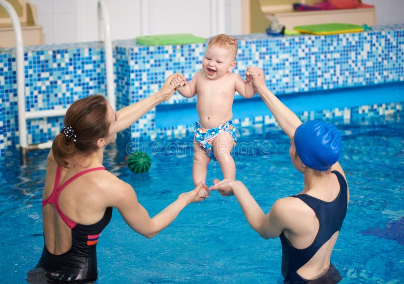 Twee vrouwen met een gelukkig lachende baby die tijdens hun zwemlessen water in de lucht sporten Baby's ontspannen in zwembad stock foto Twee vrouwen met een gelukkig lachende baby die tijdens hun zwemlessen water in de lucht sporten Baby's ontspannen in zwembad stock foto
