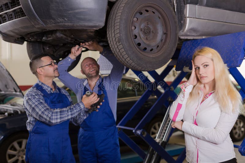 Twee werktuigkundigen die cliënt op workshop proberen te bedriegen stock fotografie Twee werktuigkundigen die cliënt op workshop proberen te bedriegen stock fotografie