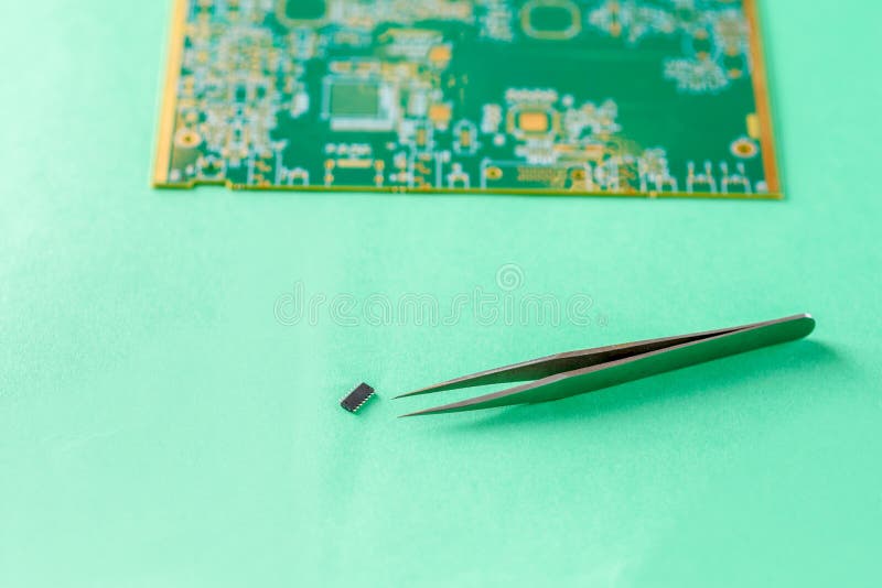 Tweezers, Computer chip and blurred small PCB-printed circuit board on green background. stock photo