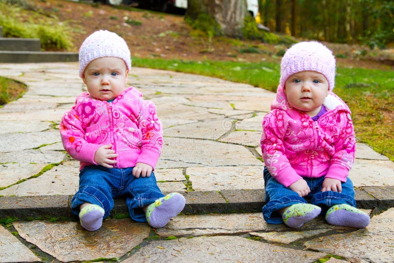 Dos mellizo un nino las chicas sentarse sobre el piedra acera agotador rosa sudaderas sombreros.