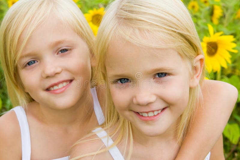 Portrait of cute girl embracing her twin sister and both looking at camera with smiles. Portrait of cute girl embracing her twin sister and both looking at camera with smiles
