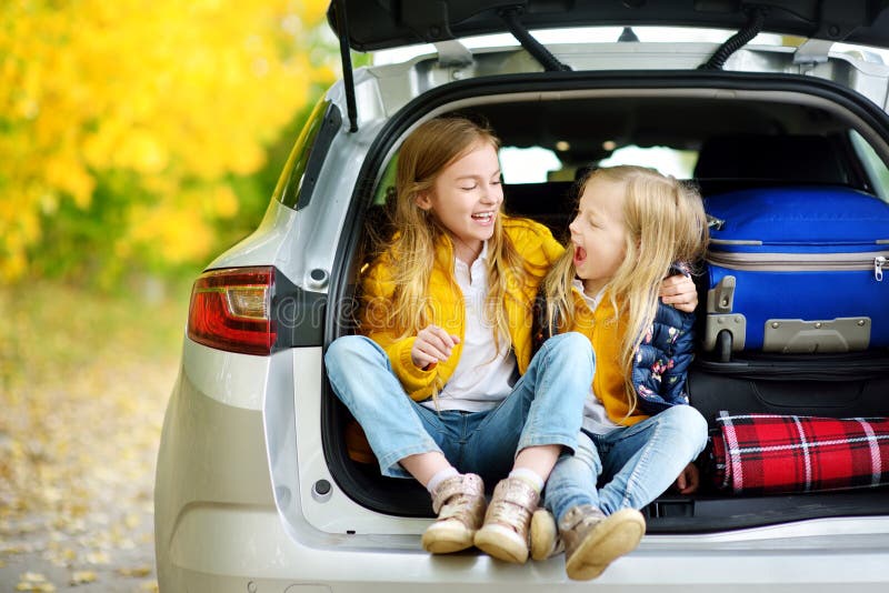 Two adorable girls sitting in a car trunk before going on vacations with their parents. Two kids looking forward for a road trip o